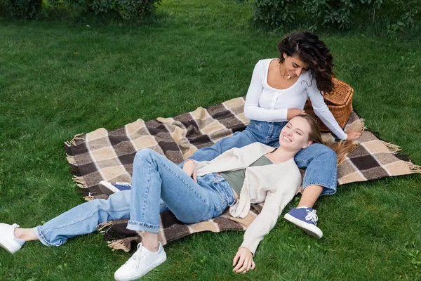 Alegre lesbiana acariciando pelo de novia acostado en a cuadros manta durante picnic - foto de stock