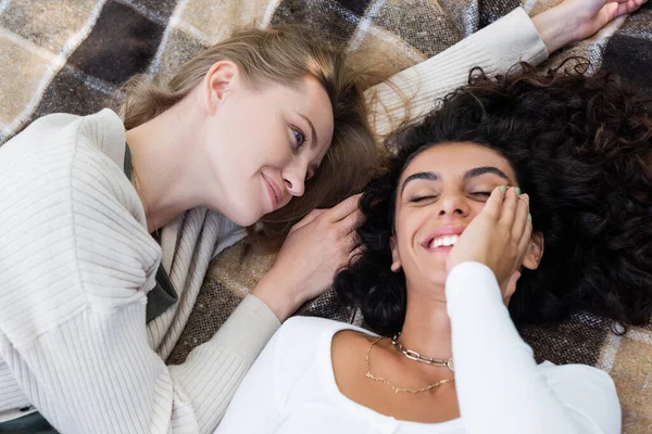 Vue du dessus du couple lesbien joyeux couché sur une couverture à carreaux pendant le pique-nique — Photo de stock