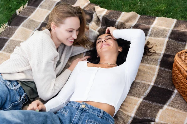 Alegre pareja lesbiana acostado en a cuadros manta durante el picnic - foto de stock