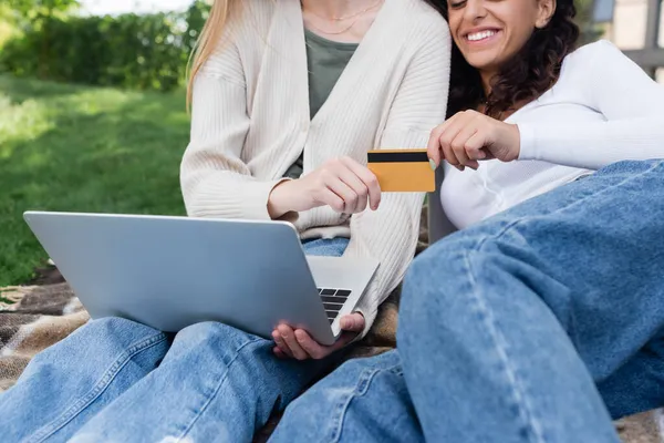 Cropped view of happy women holding credit card while doing online shopping during picnic — Stock Photo