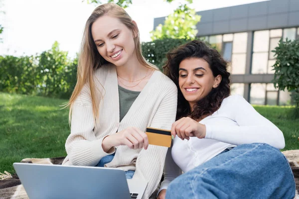 Heureux couple lesbien tenant carte de crédit tout en faisant des achats en ligne pendant le pique-nique — Photo de stock