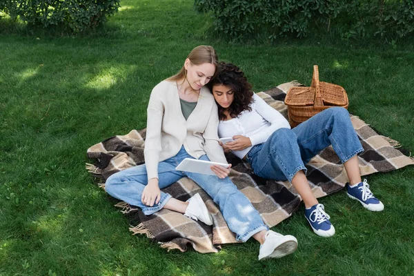 Молодые лесбиянки используют гаджеты во время пикника — стоковое фото
