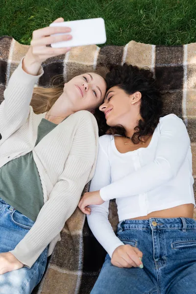 Vista ad alto angolo di donne che prendono selfie mentre si trovano sulla coperta a quadri — Foto stock