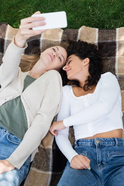 High angle view of women taking selfie while lying on plaid blanket — Stock Photo