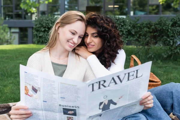 Feliz pareja lesbiana leyendo el periódico de viaje en el parque - foto de stock