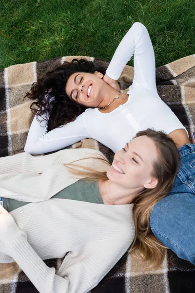 Vista superior de mujeres lesbianas complacidas tumbadas en manta a cuadros - foto de stock