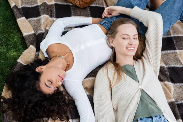 Draufsicht auf junge und zufriedene lesbische Frauen, die auf karierter Decke liegen — Stockfoto