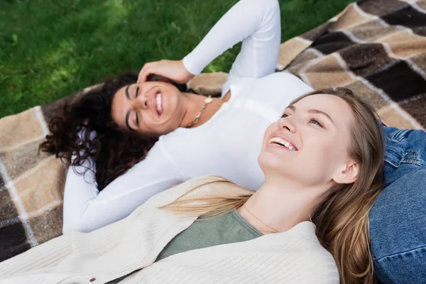 Fröhliche Freundinnen auf karierter Decke liegend — Stockfoto