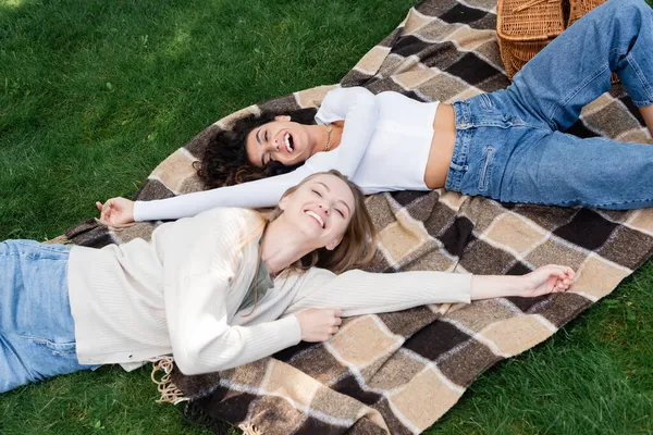 Blick aus der Vogelperspektive auf fröhliche lesbische Frauen, die auf einer karierten Decke neben dem Korb liegen — Stockfoto