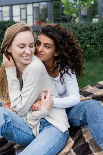 Fröhliche lesbische Frauen, die sich auf karierter Decke umarmen — Stockfoto