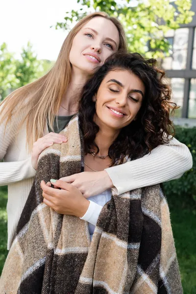 Cheerful lesbian woman covering girlfriend in plaid blanket — Stock Photo