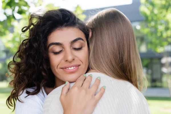 Heureux et bouclé femme étreignant petite amie à l'extérieur — Photo de stock