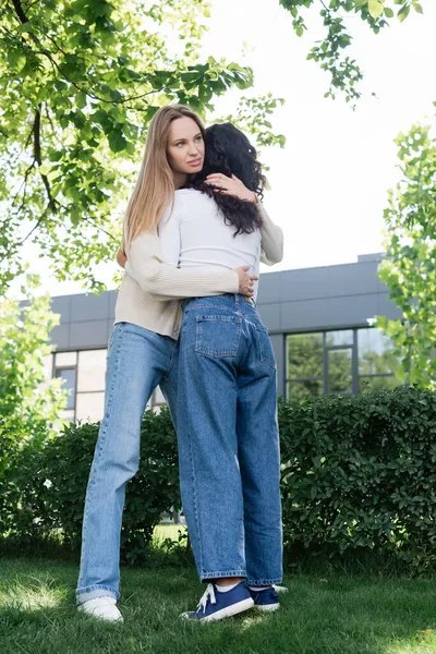 Full length of young woman hugging curly girlfriend outside — Stock Photo