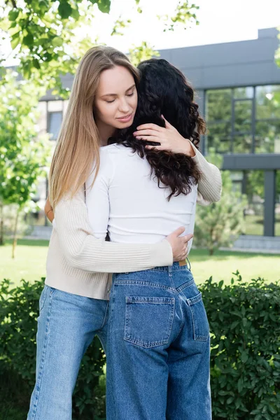 Jeune femme avec les yeux fermés étreignant petite amie bouclée à l'extérieur — Stock Photo