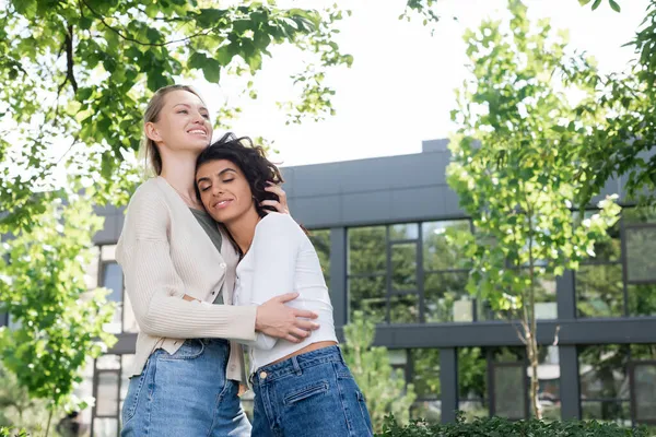 Smiling young woman hugging curly girlfriend outside — Stock Photo