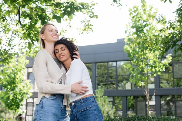 Sourire jeune femme étreignant petite amie bouclée à l'extérieur — Photo de stock