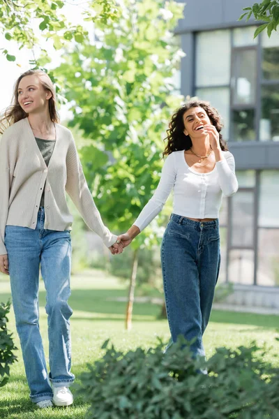 Full length of pleased lesbian couple holding hands while walking outside — Stock Photo
