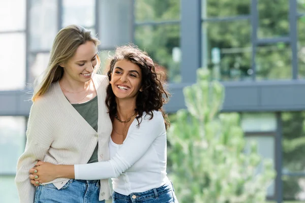 Curly woman smiling while hugging girlfriend outside — Stock Photo