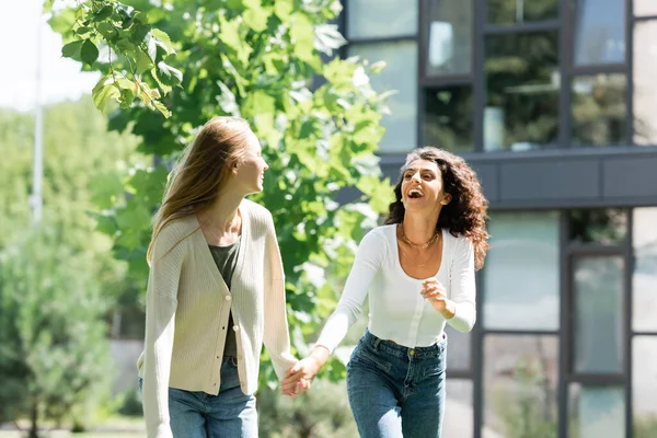 Zufriedenes lesbisches Paar hält Händchen und lacht draußen — Stockfoto