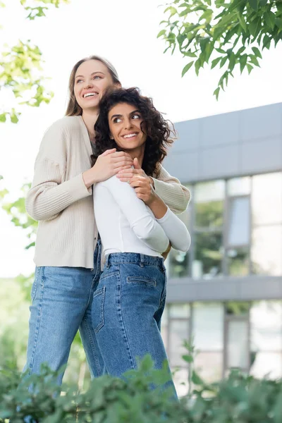 Sonriente mujer abrazando rizado joven novia fuera - foto de stock