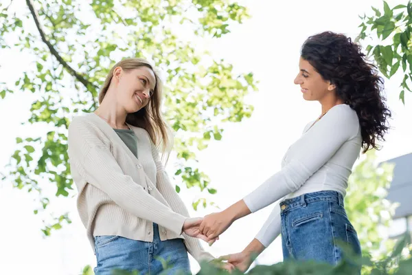 Complacida pareja del mismo sexo tomados de la mano y mirándose fuera - foto de stock