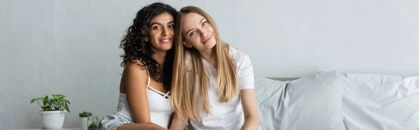 Happy same sex couple looking at camera in bedroom, banner — Stock Photo