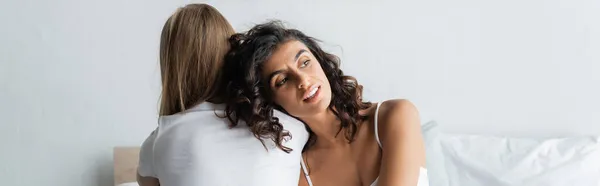Mujer rizada apoyada en el hombro de la novia en casa, pancarta — Stock Photo