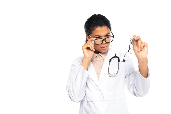 Médico afro-americano focado olhando para óculos isolados em branco — Fotografia de Stock