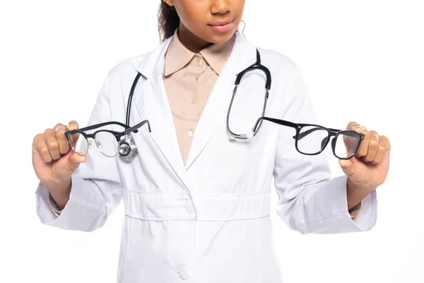 Cropped view of african american oculist in white coat and stethoscope holding eyeglasses isolated on white — Stock Photo