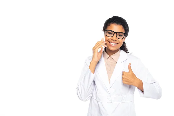 Jeune médecin afro-américain en lunettes parlant sur smartphone et montrant comme isolé sur blanc — Photo de stock