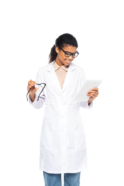 African american oculist in white coat holding digital tablet and eyeglasses isolated on white — Stock Photo