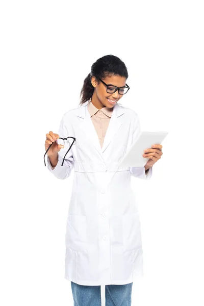 Afro-Américain oculiste en manteau blanc tenant tablette numérique et lunettes isolées sur blanc — Photo de stock