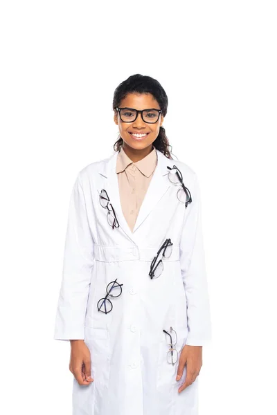 Oculiste afro-américain souriant dans des lunettes sur le manteau en regardant la caméra isolée sur blanc — Photo de stock