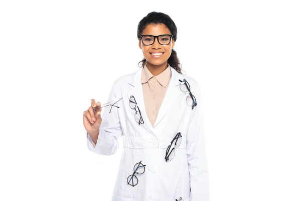 Médecin afro-américain positif avec des lunettes sur le manteau regardant la caméra isolée sur blanc — Photo de stock