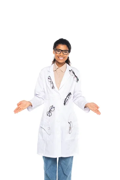 Lächelnder afrikanisch-amerikanischer Augenarzt mit Brille auf weißem Mantel zeigt mit isolierten Händen auf weißem Grund — Stockfoto