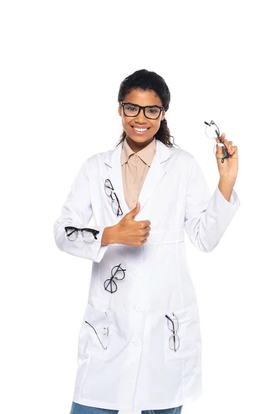 Позитивный африканский американский врач в очках на белом халате показывает большой палец вверх жест изолирован на белом — стоковое фото