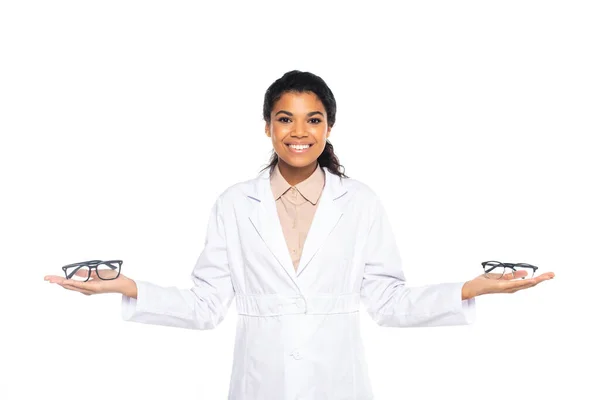 Jolie médecin afro-américain tenant des lunettes sur les mains et regardant la caméra isolée sur blanc — Photo de stock