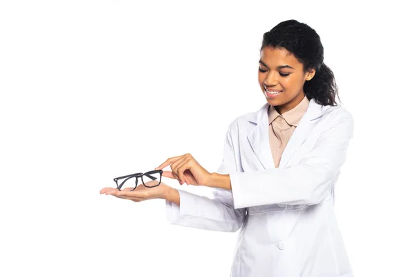 Jolie ophtalmologiste afro-américain souriant regardant des lunettes isolées sur blanc — Photo de stock