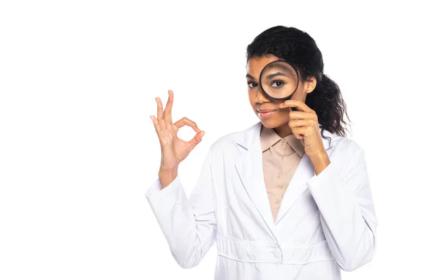 African american oculist holding magnifying glass and showing ok sign isolated on white — Stock Photo