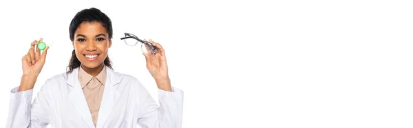 Happy african american doctor holding optical lenses and eyeglasses isolated on white with copy space, banner — Stock Photo