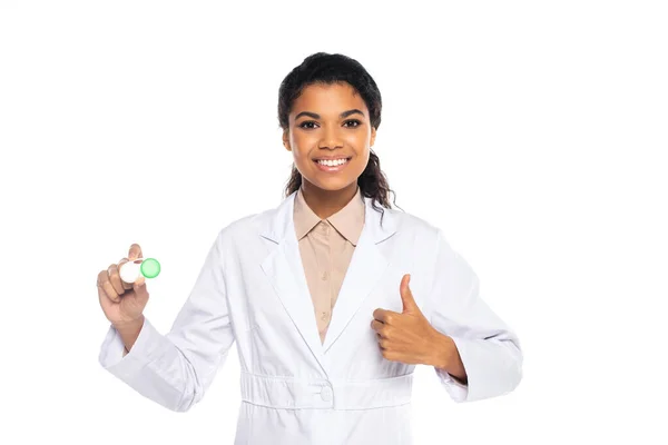 Lächelnder afrikanisch-amerikanischer Arzt im weißen Mantel, der Behälter mit Linsen hält und den Daumen vereinzelt auf weiß zeigt — Stockfoto