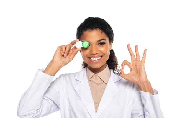 Joyeux médecin afro-américain tenant des lentilles de contact et montrant ok signe isolé sur blanc — Photo de stock