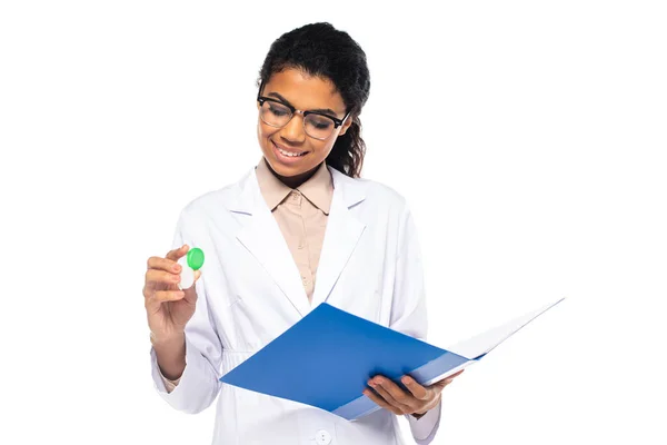 Médecin afro-américain souriant dans des lunettes tenant des lentilles de contact et un dossier en papier isolé sur blanc — Photo de stock