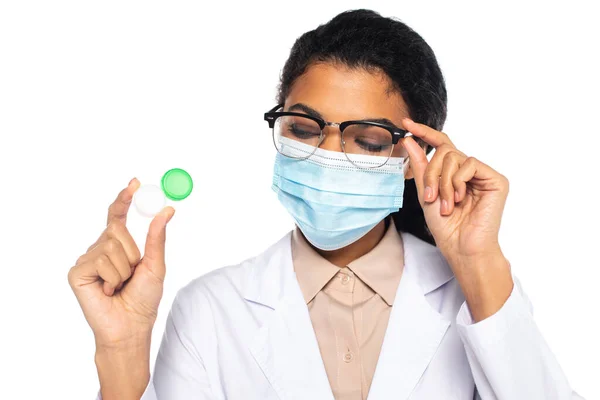 Ophtalmologiste afro-américain en masque médical et lunettes tenant les lentilles de contact isolées sur blanc — Photo de stock