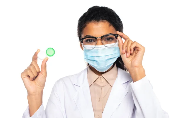 Medico afroamericano in occhiali da vista e maschera medica contenente contenitore con lenti isolate su bianco — Foto stock