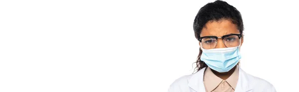 Расстроенный африканский американский врач в медицинской маске и очках, глядя на камеру, изолированную на белом, баннер — стоковое фото
