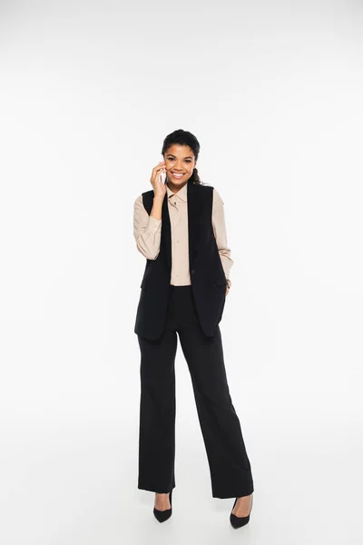 Piena lunghezza di sorridente donna d'affari afro-americana che parla su smartphone su sfondo bianco — Foto stock