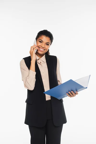 Joven mujer de negocios afroamericana hablando en un teléfono inteligente y sosteniendo una carpeta de papel aislada en blanco - foto de stock