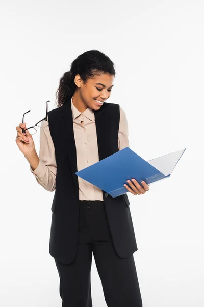 Cheerful african american businesswoman holding eyeglasses and paper folder isolated on white — Stock Photo