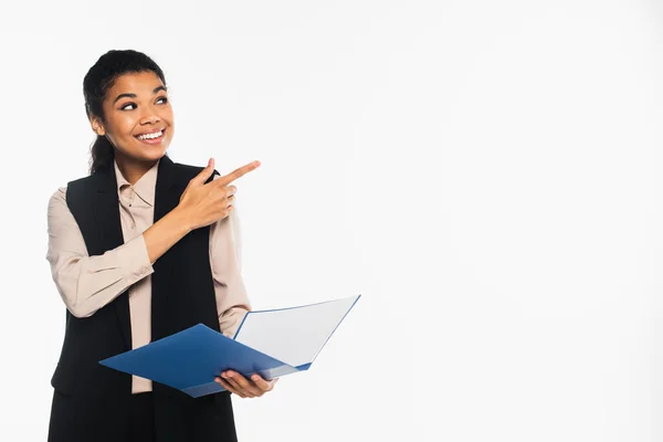 Sonriente mujer de negocios afroamericana sosteniendo la carpeta de papel y señalando con el dedo aislado en blanco - foto de stock